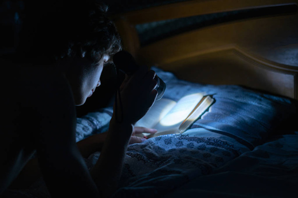 nuori henkilö kevyen taskulampun kanssa lukemassa kirjoja sängyssä yöllä makuuhuoneissa
 - Valokuva, kuva
