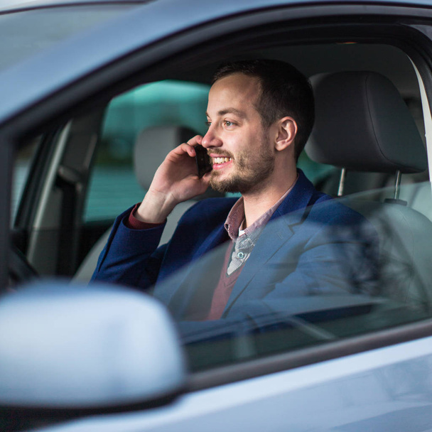 Pohledný mladý muž, který se dívá na mobil, zatímco u volantu  - Fotografie, Obrázek