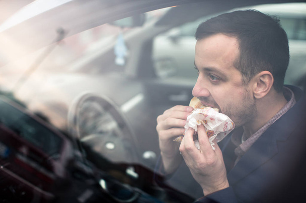 Csinos fiatal ember eszik egy sietős ebéd a kocsijában  - Fotó, kép