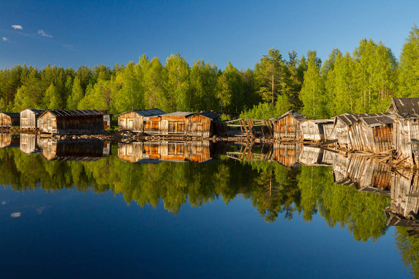 Old wooden boat sheds on Lake Kovdozero in the Murmansk region, Zelenoborsky village. The reflection in the water of trees and boat garages - Photo, Image