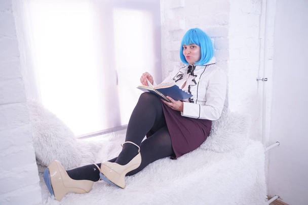 όμορφο συν μέγεθος κορίτσι σε μπλε περούκα έχουν πολλά όνειρα με το ημερολόγιό της μόνο κάθεται σε λευκό περβάζι - Φωτογραφία, εικόνα