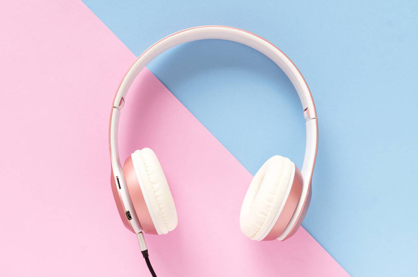 Pink headphone and black cable on pastel color blue and pink background. Music concept. - Фото, изображение