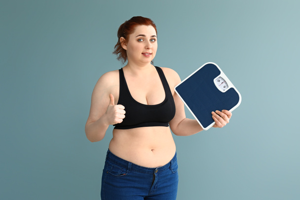 Túlsúlyos nő mérlegek mutató hüvelykujj-up a színes háttér. Testsúlycsökkenés koncepció - Fotó, kép