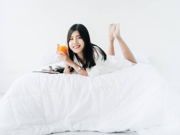 Asian woman drinking a glass of orange juice on bed at home, lif - Фото, зображення