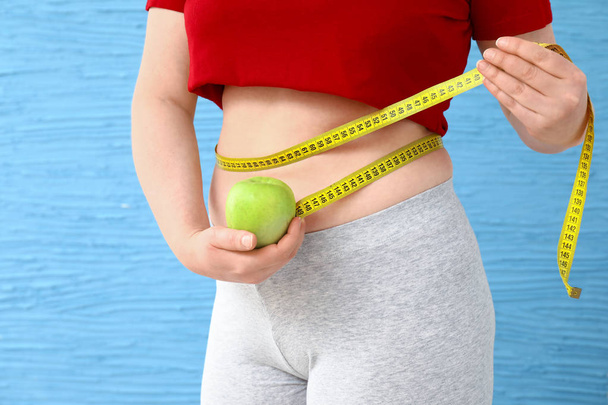 Mujer con sobrepeso con manzana y cinta métrica sobre fondo de color. Concepto de pérdida de peso
 - Foto, imagen