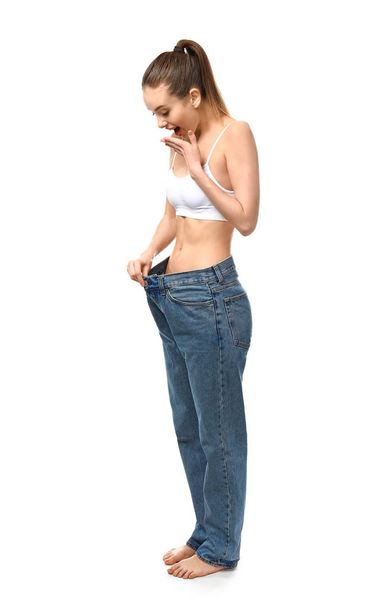 Happy young woman in loose jeans on white background. Weight loss concept - Zdjęcie, obraz
