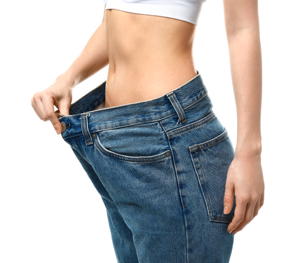 Jonge vrouw in losse jeans op witte achtergrond. Gewichtsverlies concept - Foto, afbeelding