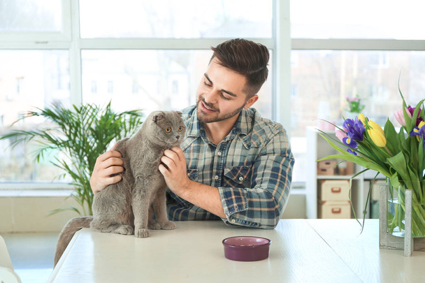 Young man feeding cute funny cat at home - Photo, Image