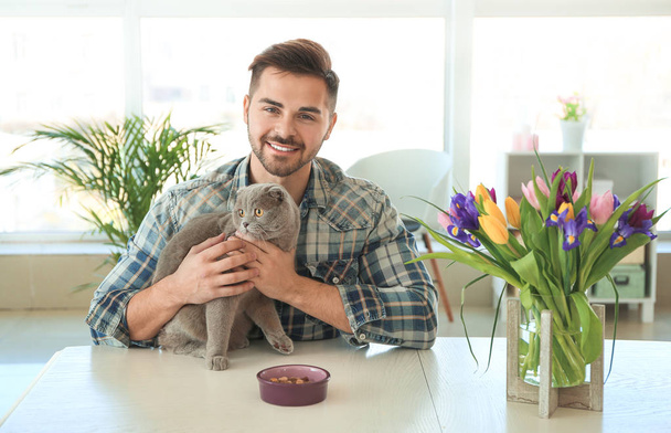 Young man feeding cute funny cat at home - Photo, Image
