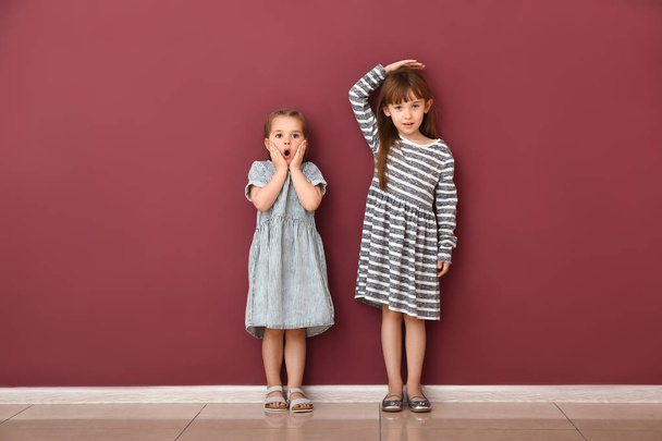 Pienet tytöt mittaavat korkeutta seinän lähellä
 - Valokuva, kuva