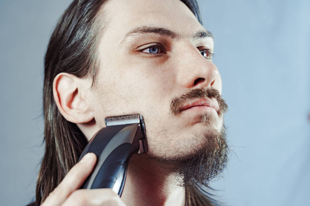 Парень сбривает бороду электрической бритвой
 - Фото, изображение