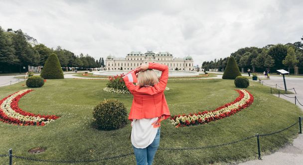 Adult caucasian woman holding Austrian flag on Belvedere palace background - Fotoğraf, Görsel