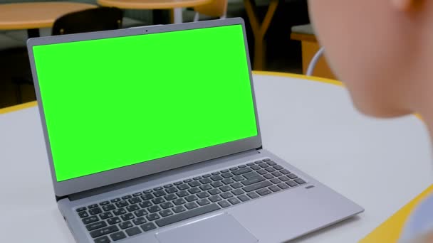 Γυναίκα κοιτάζοντας φορητό υπολογιστή με κενή πράσινη οθόνη στο καφέ - Πλάνα, βίντεο