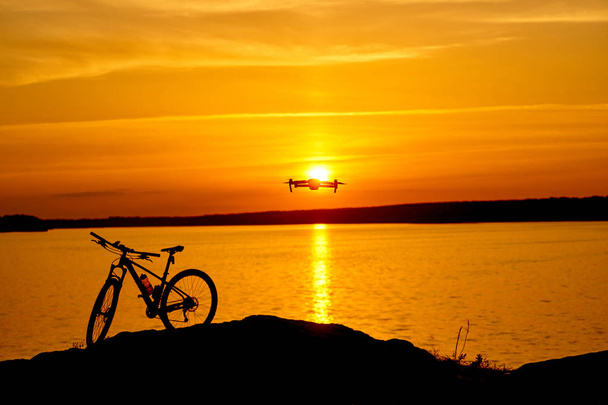 silhouette of a bicycle at sunset. drone quadcopter with digital camera flying at sunset - Фото, изображение