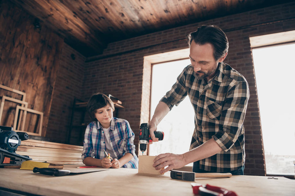 Portrait of charming nice pretty focused son father hold hand have equipment craftsmen apprentice diy teacher workplace home hobby wear checkered shirt beard studio industrial interior - 写真・画像