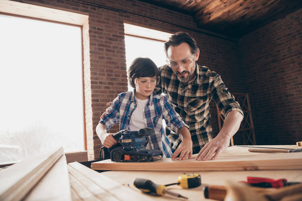 Low angle view of two nice focused concentrated inspired person master builder dad teaching son explaining training fixing repairing building cabinetry restoration at studio loft industrial style - Photo, image