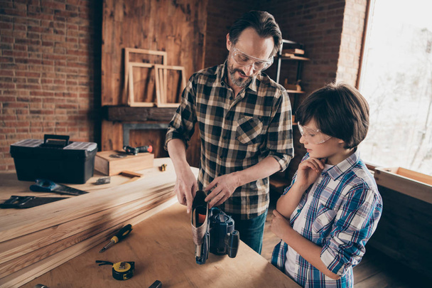 Portrait of two nice person focused cheerful woodworkers master handyman dad daddy teaching son industry interesting profession at modern loft industrial brick interior - Foto, Imagem