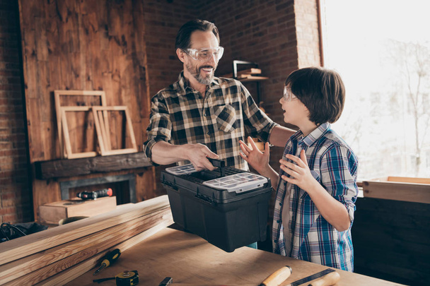 Portrait of two nice person cheerful cheery glad woodworkers master handyman dad giving new cool toolbox toolkit to son production at modern loft industrial brick interior - Foto, afbeelding