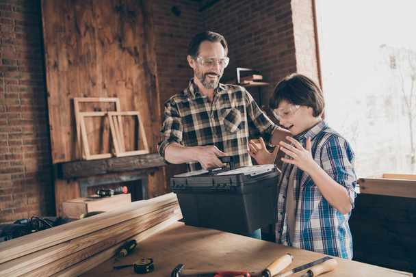 Portrait of two nice person cheerful cheery glad successful woodworkers master handyman dad giving new toolkit to son production industry at modern loft industrial brick interior - 写真・画像