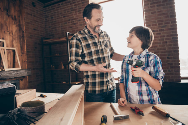 Portrait of two nice person cheerful woodworkers master handyman sharing experience skills showing how to use electrical device at modern loft industrial brick interior indoors - Foto, imagen