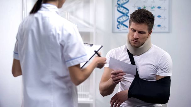 Patient in foam cervical collar and arm sling reading doctors prescription - Foto, afbeelding