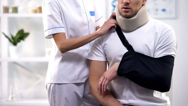 Female surgeon adjusting male patient arm sling, orthopedics and rehab period - Fotografie, Obrázek