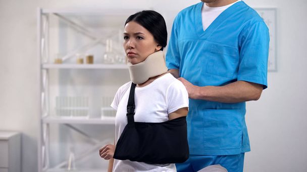 Professional male surgeon fixing arm sling upset patient in foam cervical collar - Photo, Image