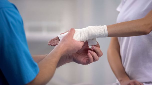 Orthopedist applying wrist elastic wrap on female patient hand joint dislocation - Foto, afbeelding