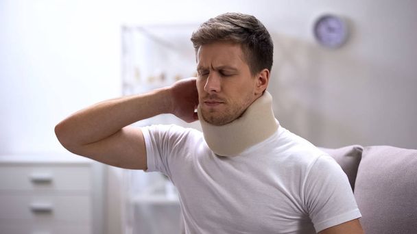 Displeased man in foam cervical collar suddenly feeling pain in neck, trauma - Photo, Image