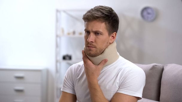 Sad male in foam cervical collar touching neck, feeling upset after trauma - Fotografie, Obrázek