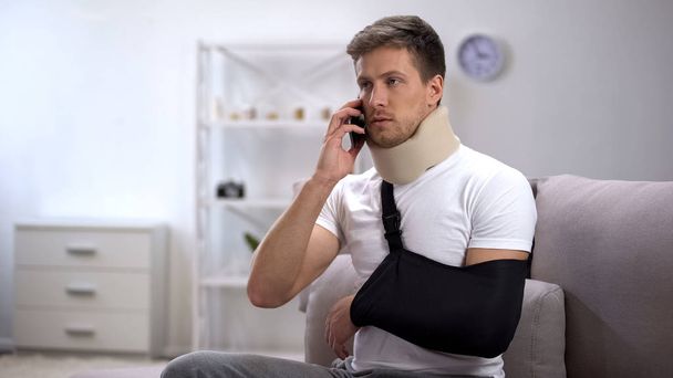 Man in arm sling and foam cervical collar talking on cellphone, upset with news - Zdjęcie, obraz