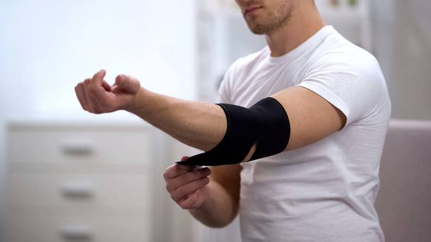Young male applying elbow padded orthosis, orthopedics and physiotherapy, health - Fotografie, Obrázek