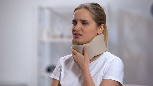 Girl in foam cervical collar touching neck, suffering from pain, recovery - Foto, immagini