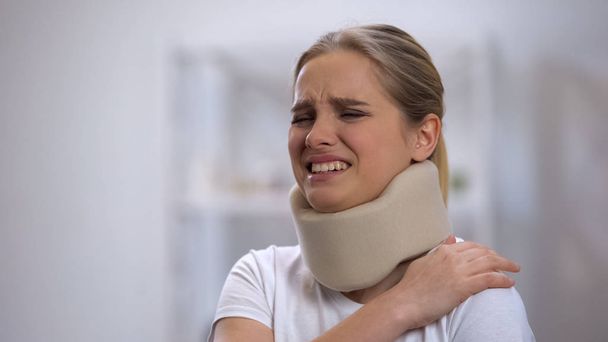 Upset girl in foam cervical collar suffering pain in shoulder, accident injury - Foto, imagen