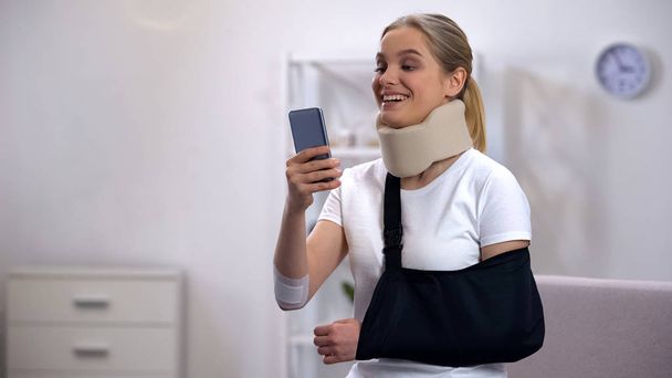 Cheerful woman in foam cervical collar and arm sling chatting on cellphone rehab - Zdjęcie, obraz