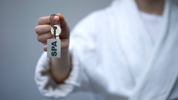 Mujer en albornoz sosteniendo llaves con palabra SPA, servicios de recreación en el hotel
 - Foto, imagen