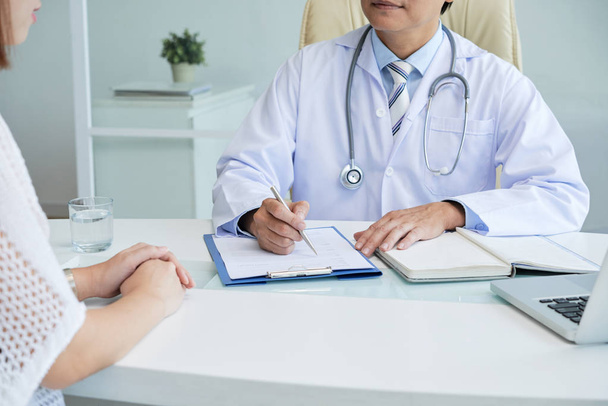 Cropped image of doctor filling medical paper for his female client - Photo, Image