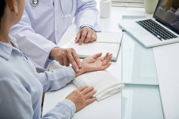 Lekarz dotyka nadgarstka kobiece pacjenta, aby sprawdzić puls - Zdjęcie, obraz