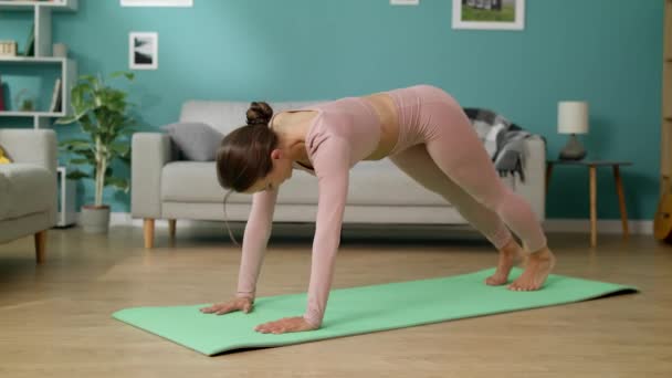 Jovem mulher se exercitando em casa praticando postura de cão voltado para baixo em casa
 - Filmagem, Vídeo