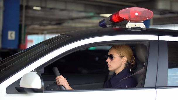 Female cop driving police car in underground parking, patrolling, law and order - Φωτογραφία, εικόνα