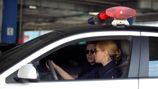 Mies ja nainen poliisi ajavat poliisiautolla rikospaikalle, partioivat lakia kaupungissa
 - Valokuva, kuva