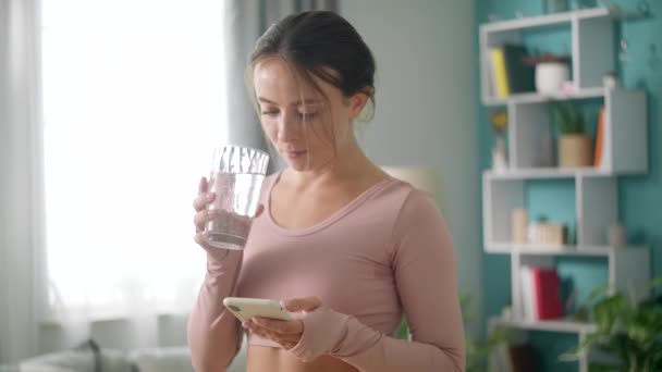 Young woman is drinking water after training on the home interior - Filmmaterial, Video