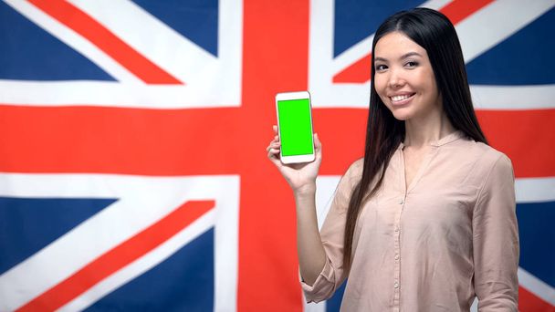Señora mostrando el teléfono con pantalla verde contra la bandera británica en el fondo, aplicación
 - Foto, imagen