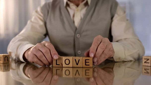 Senior man making word love of wooden cubes on table, memory disease, health - Foto, Imagen