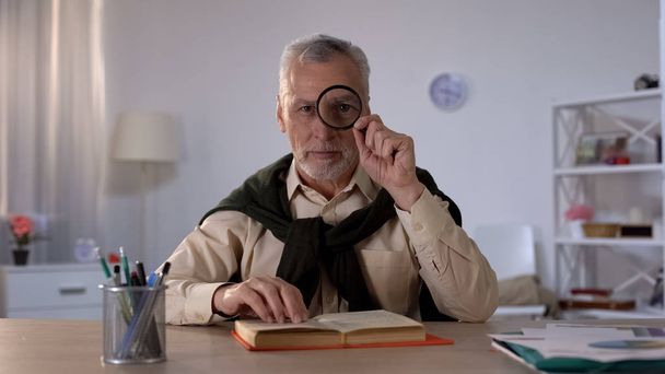 Old man looking through magnifying glass, free time with pleasure, enlarged eye - Фото, изображение