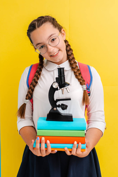 Portrait of a schoolgirl in glasses with books textbooks on a yellow blue background in the Studio. - Φωτογραφία, εικόνα