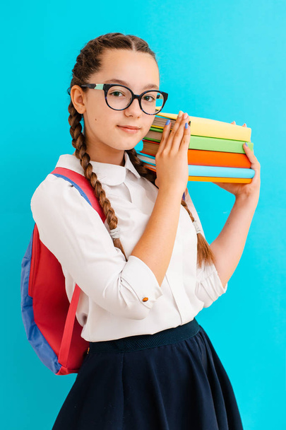 Portré egy iskolás lány szemüvegben könyvek tankönyvek sárga kék háttér a stúdióban. - Fotó, kép