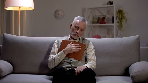 Elderly man sleeping on couch with book in hands, leisure time on weekends - 写真・画像