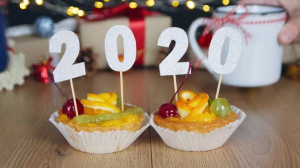 Happy New Year 2020. Happy New Year's berries cupcakes with 2020 numbers take away female and male hands on bokeh Christmas fairy lights background. - Video, Çekim