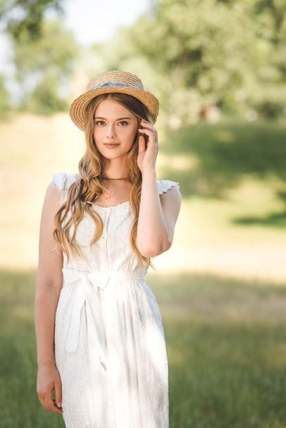 beautiful girl with straw hat standing on meadow and looking at camera - Zdjęcie, obraz